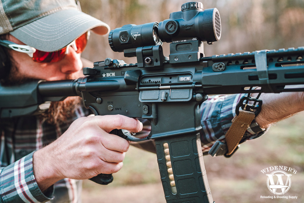 a photo of a man using a red dot magnifier on an ar-15 rifle